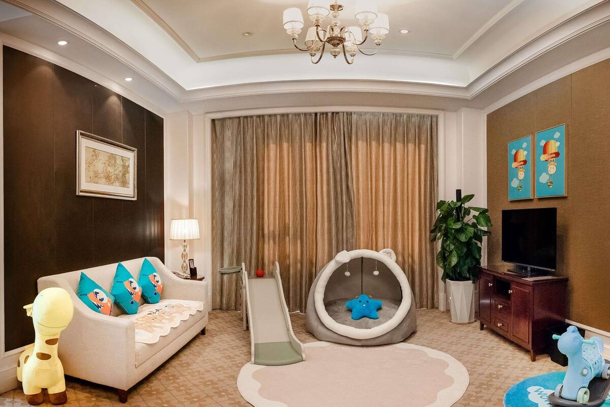 A living room with a sofa, a playpen, a slide, a giraffe toy, a television, and a plant.