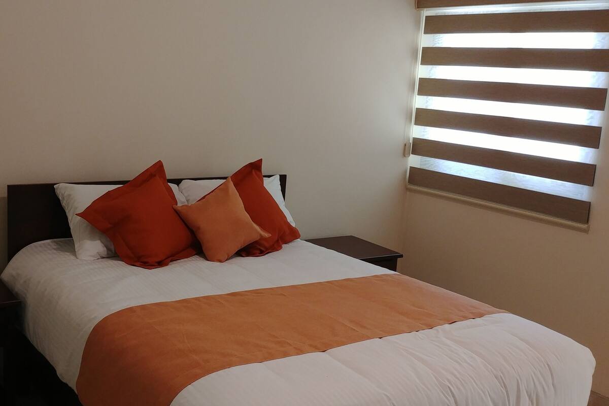 Una cama bien hecha con una colcha blanca y naranja, dos almohadas naranjas y un cabecero de madera oscura.