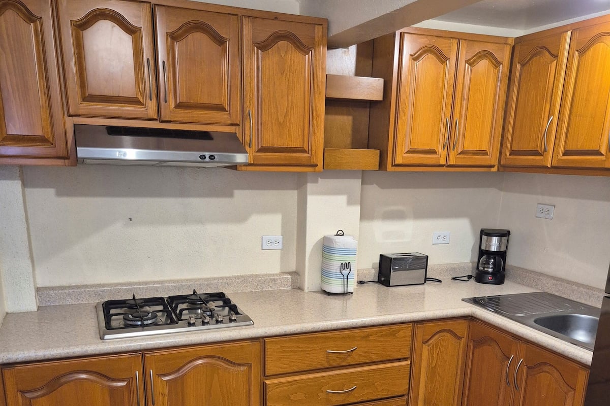 Una cocina con armarios de madera, una estufa a gas, un tostador y una cafetera.