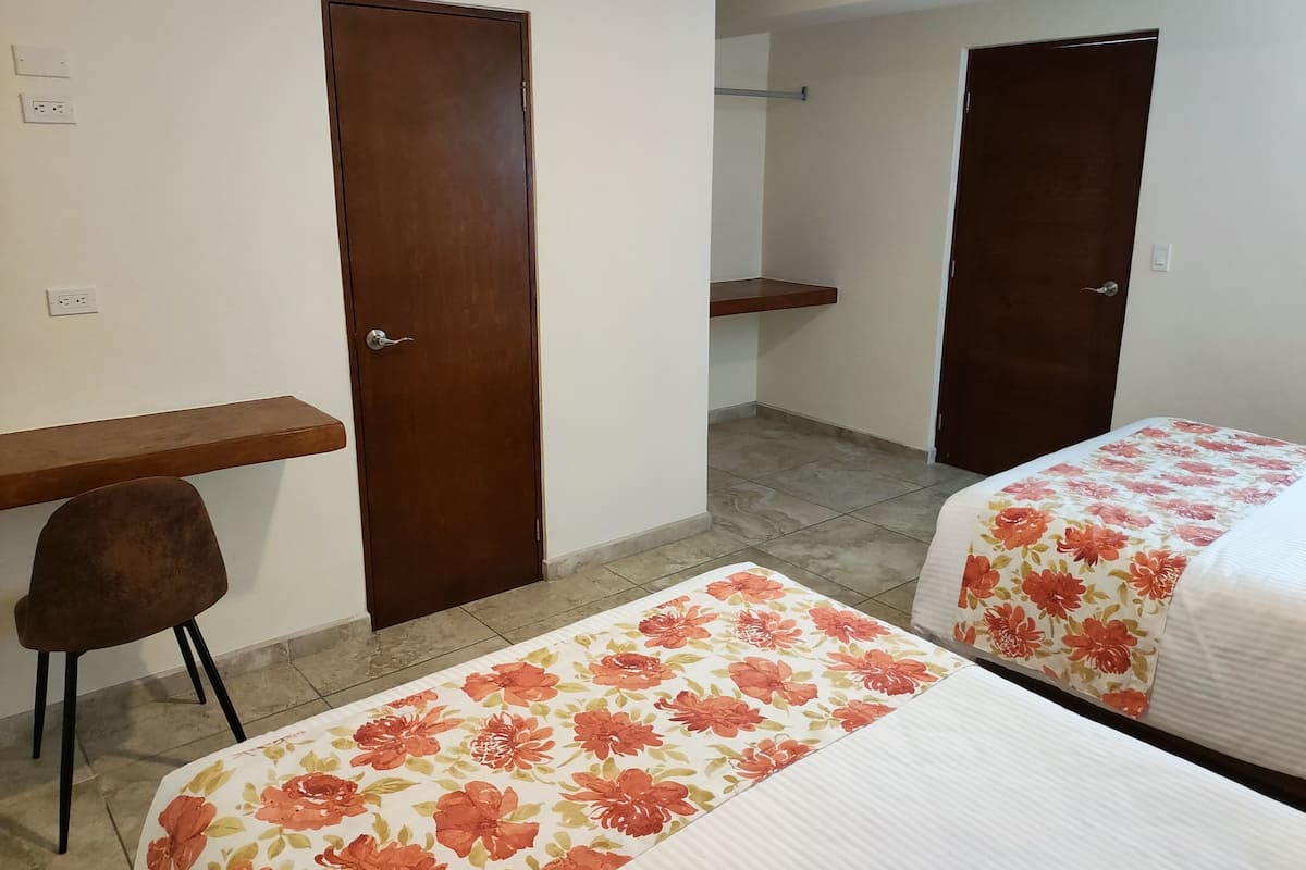 Una habitación con dos camas, un escritorio, una silla y dos puertas.