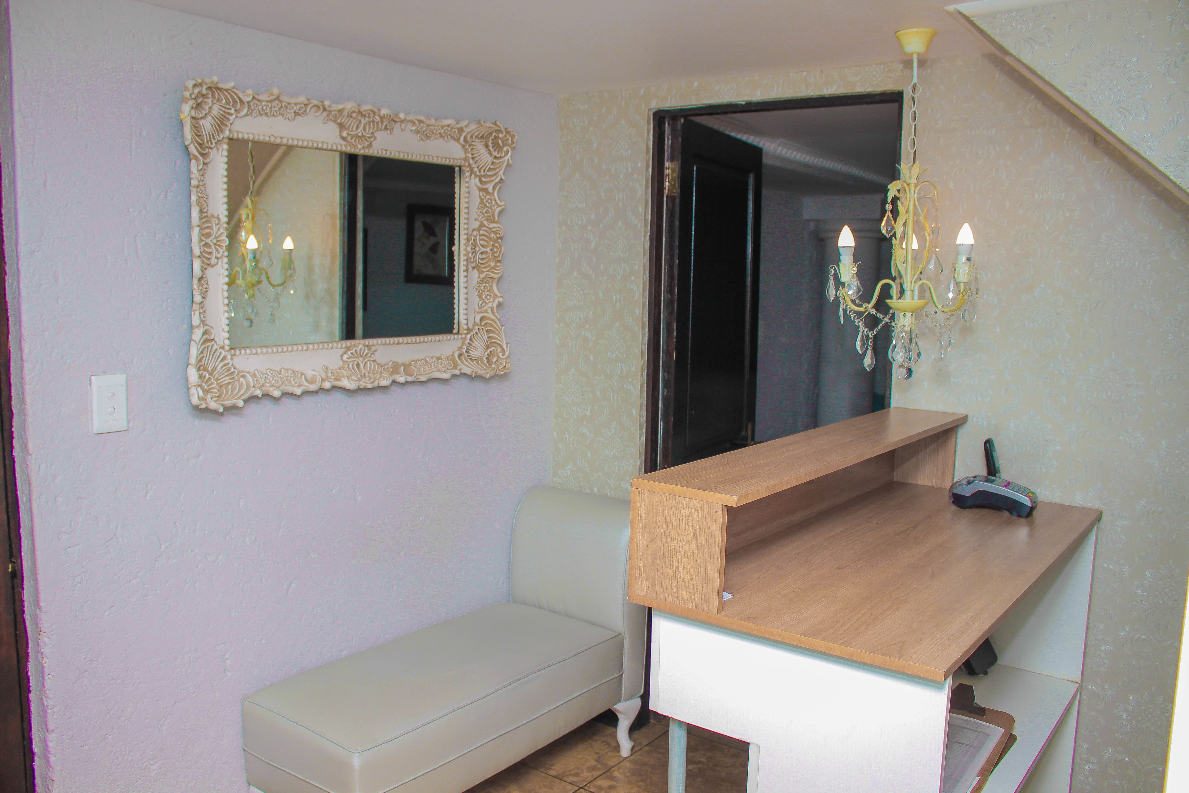 A room with a wooden desk, a bench, a mirror with an ornate frame, and a chandelier.