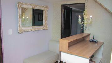 A room with a wooden desk, a bench, a mirror with an ornate frame, and a chandelier.