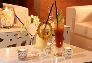 Une table où sont disposées diverses boissons, notamment une margarita, un cocktail tropical et un Bloody Mary, ainsi que de petites bougies décoratives.
