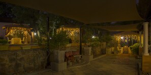 Un espace extérieur aménagé en terrasse, avec des murs en pierre, des plantes en pot et des tables placées sous une tonnelle.