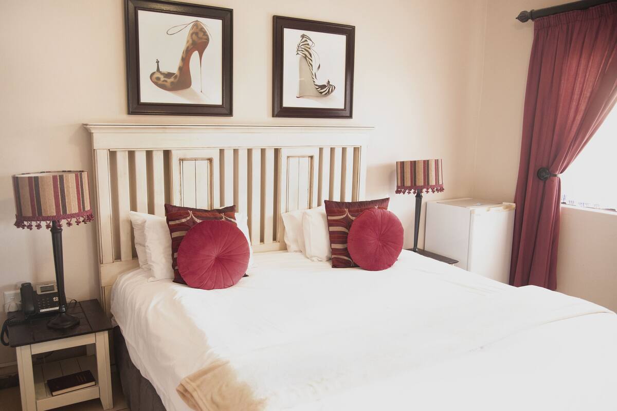 Une chambre d’hôtel avec un grand lit, deux tables de chevet avec des lampes, une tête de lit et deux tableaux encadrés au mur.