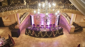 Een statig theaterpodium met weelderige decoraties, een kroonluchter en een tribune met rijen zitplaatsen.