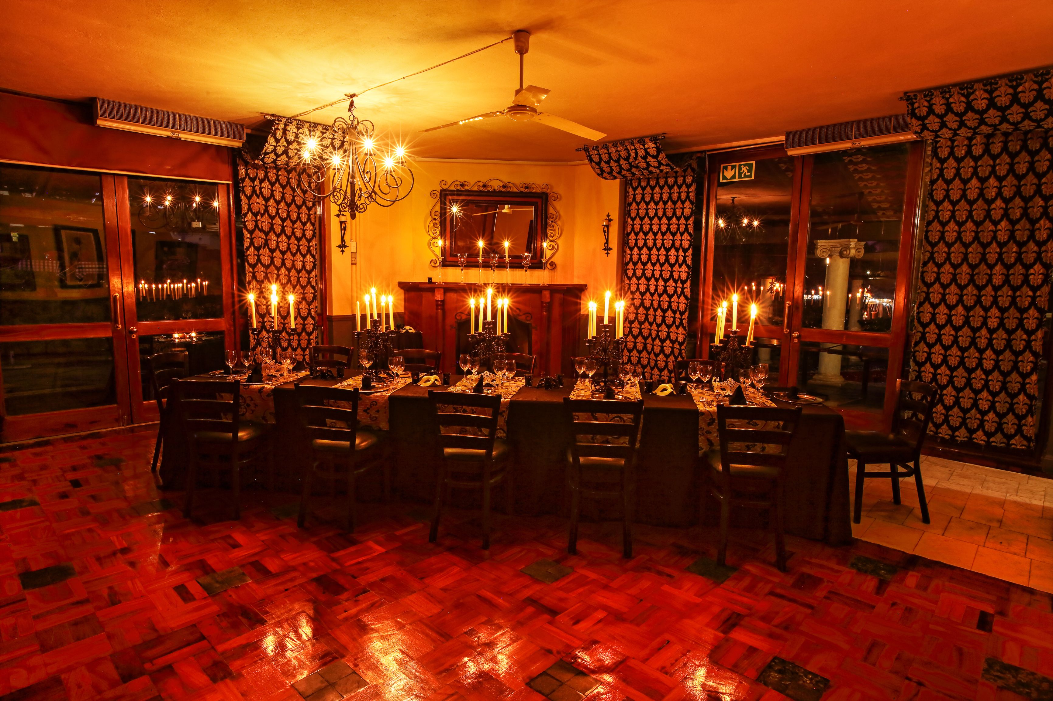 Un comedor tenuemente iluminado con una larga mesa dispuesta para una comida, velas y una araña.