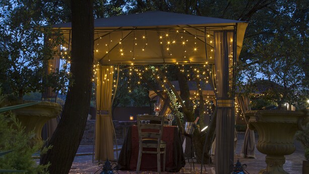 Een open tuinpaviljoen met lichtslingers, een eettafel en lantaarns aan weerszijden.