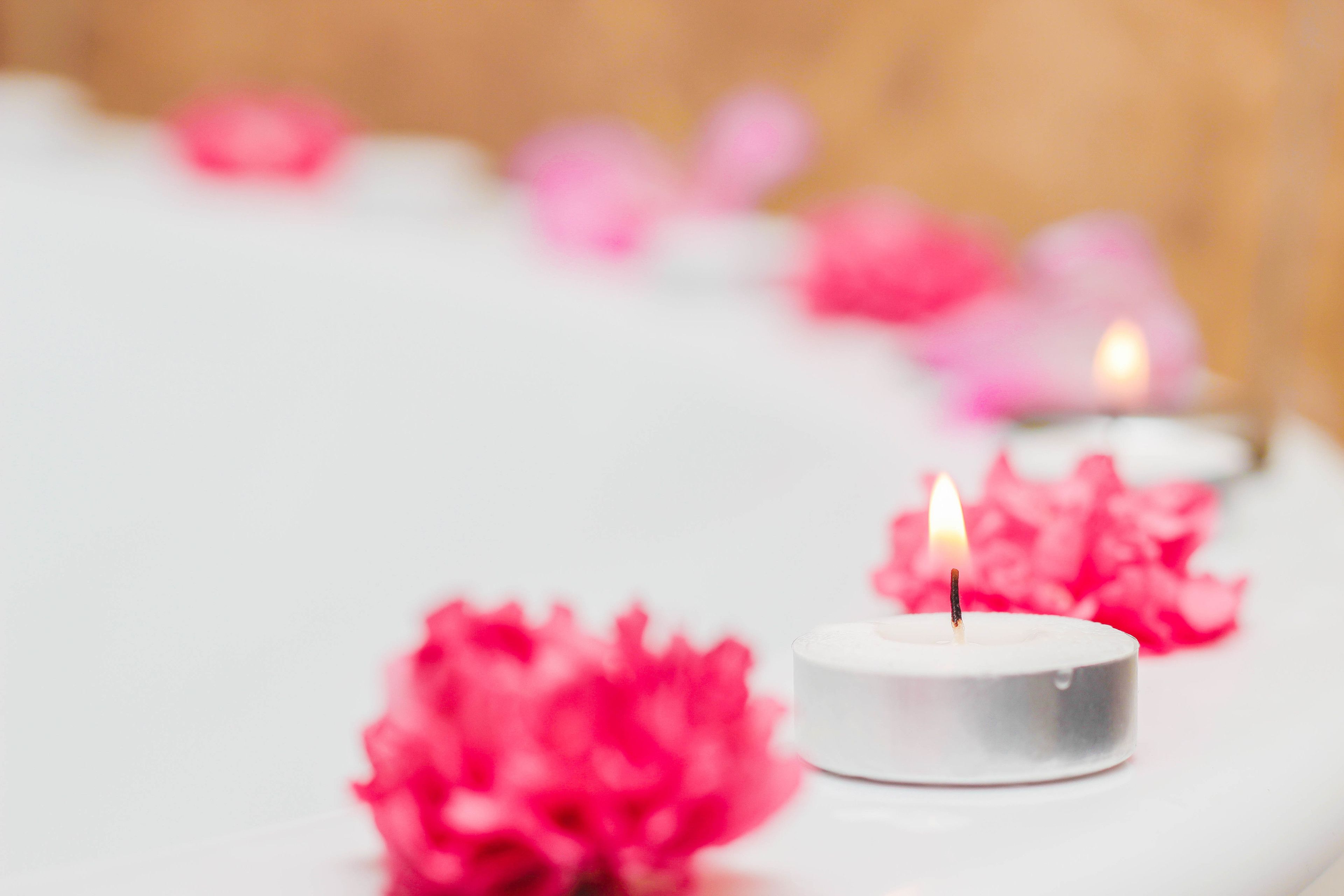 A candle with pink petals on a white surface.