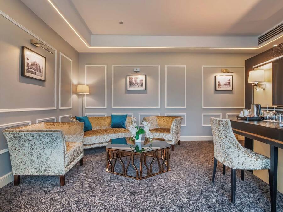 A hotel room with a sofa set, a coffee table, and a dining area.