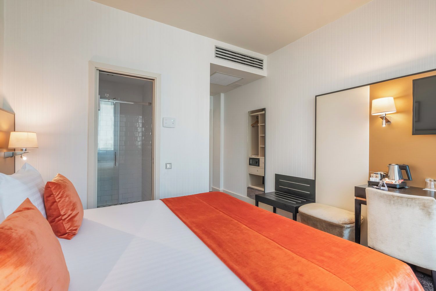 Una habitación de hotel con cama, escritorio, silla, espejo y armario.