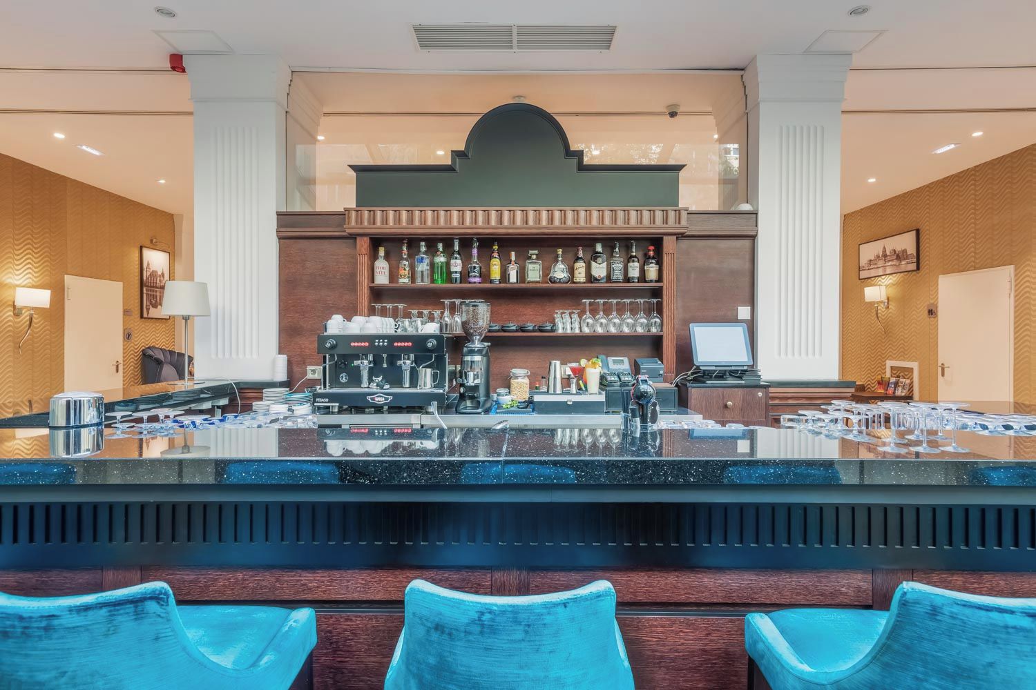 A bar area with a counter, bar stools, a coffee machine, and a shelf with bottles.