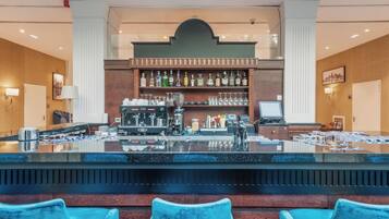 A bar area with a counter, bar stools, a coffee machine, and a shelf with bottles.