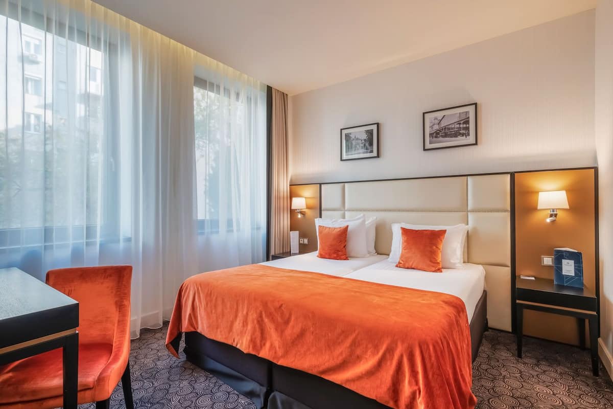 A hotel room with a bed, two bedside tables with lamps, a desk, and a chair.