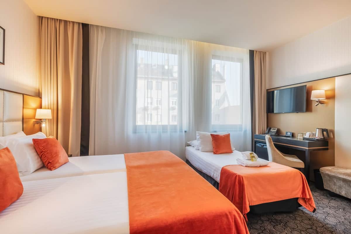 A hotel room with two beds, a desk, a chair, a TV, and a window with curtains.