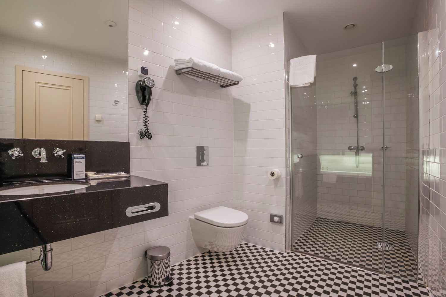 A modern bathroom with a black and white checkered floor, a glass-enclosed shower, and a black countertop with a sink and mirror.