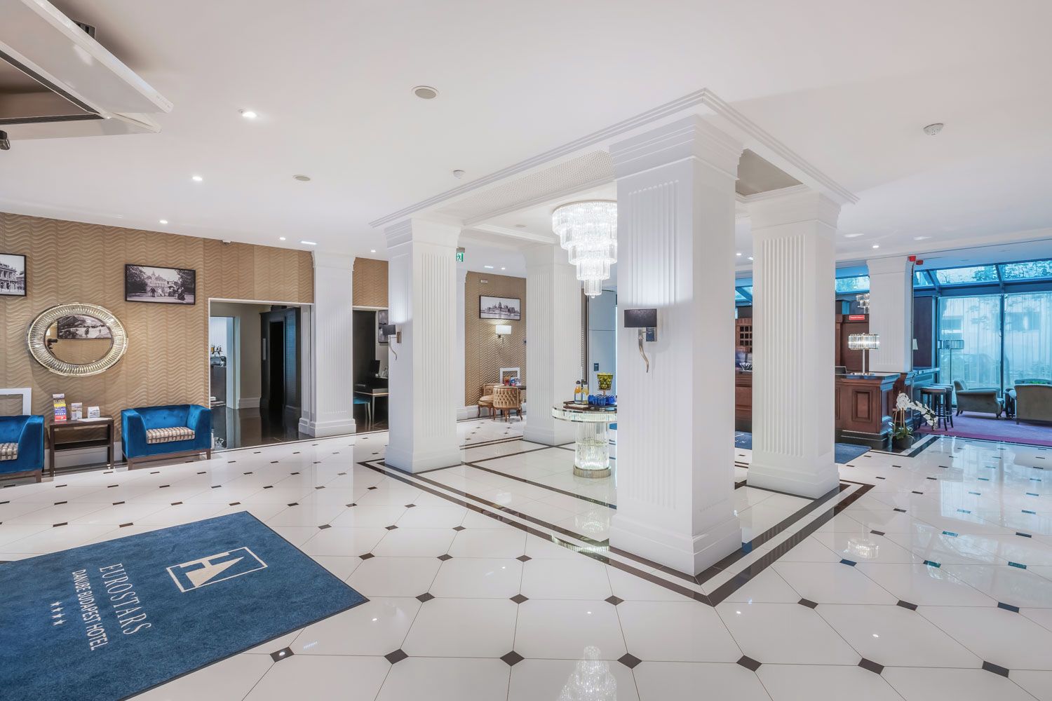 A hotel lobby with a chandelier, a reception desk, and a blue carpet with the hotel name.
