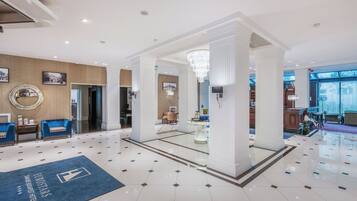 A hotel lobby with a chandelier, a reception desk, and a blue carpet with the hotel name.