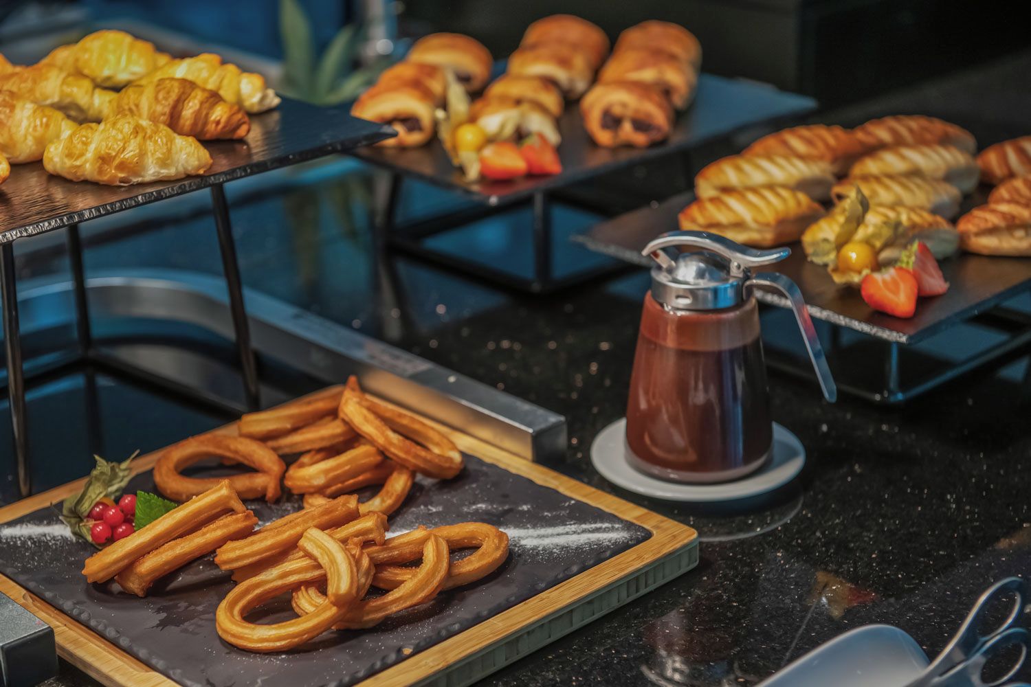 A buffet with various pastries, including croissants and pastries with fruit, and a coffee pot on a table.