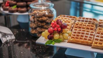 A buffet table with waffles, a jar of cookies, and a plate of grapes.