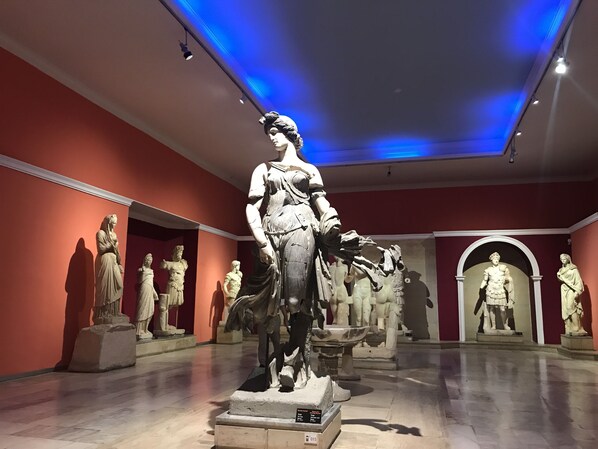 Interior de museo con estatuas clásicas exhibidas frente a paredes rojas.