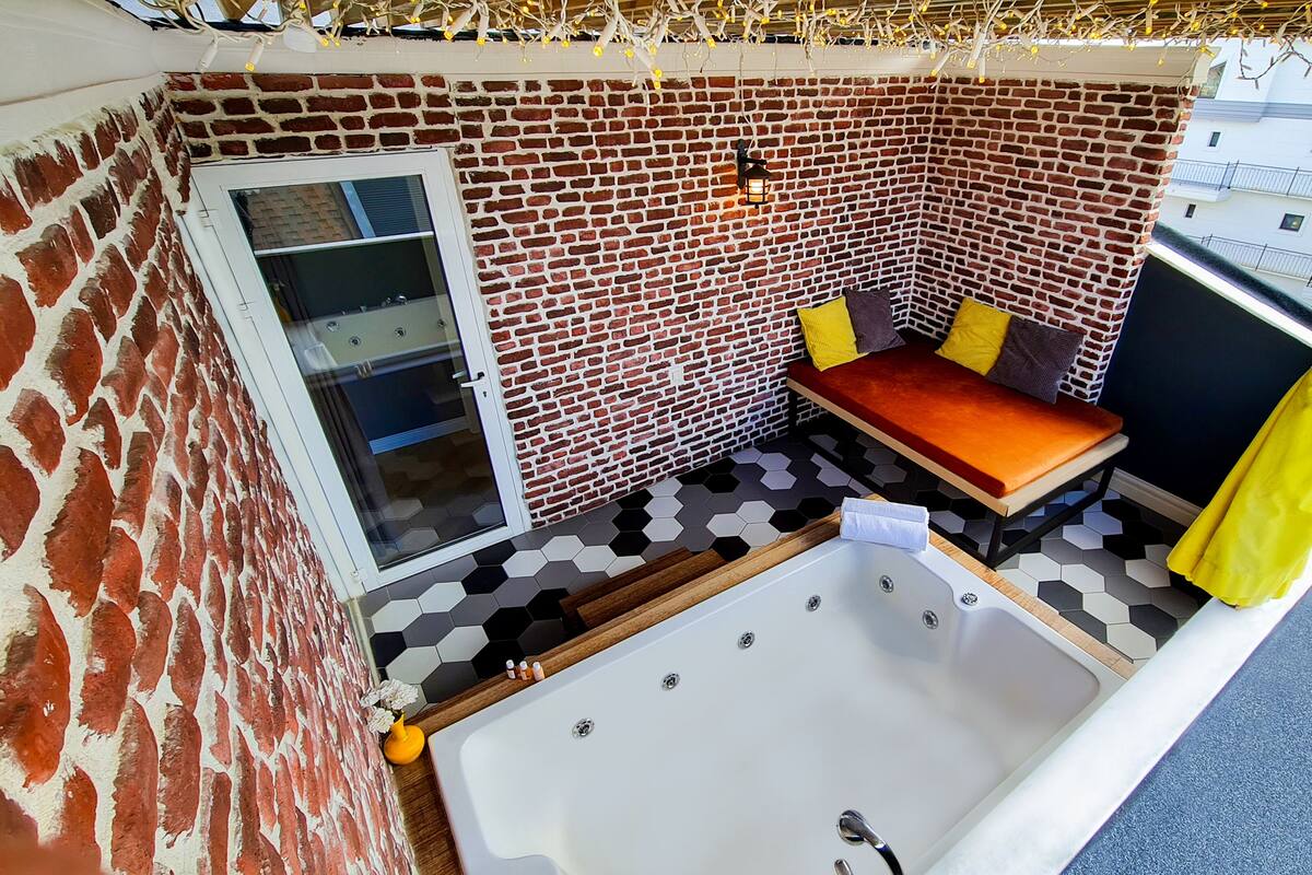 A small, cozy bathroom with a brick wall, a window, a bench, and a bathtub.