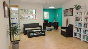 Une pièce comprenant un canapé, des fauteuils, une table basse avec des magazines, une bibliothèque, un bureau et un ordinateur.