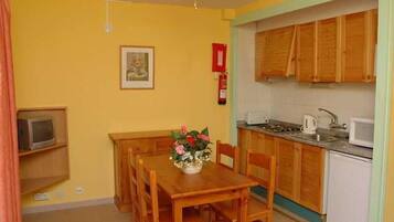 Une cuisine compacte avec des meubles en bois, une table à manger avec des chaises, une petite télévision et un ventilateur de plafond.