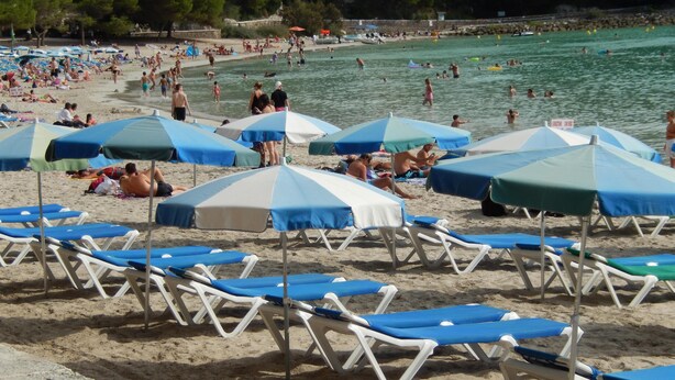 A beach with rows of sun loungers and umbrellas, a pool area, and people swimming and relaxing. - Alta Galdana (Ciutadella de Menorca)