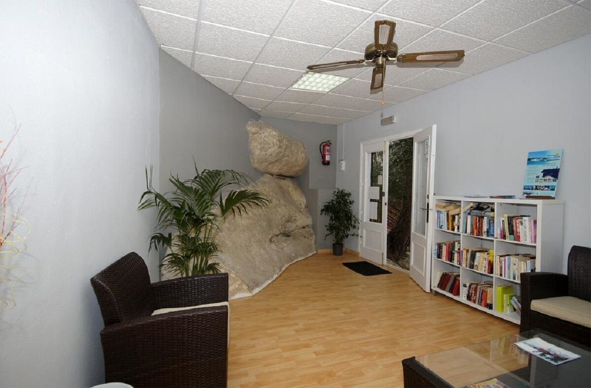 A reception area with a wooden floor, wicker furniture, a bookshelf, and a ceiling fan.