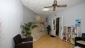 Un espace d’accueil doté d’un plancher en bois, de meubles en osier, d’une bibliothèque et d’un ventilateur de plafond.