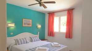 A bedroom with a bed, a ceiling fan, a window with curtains, and wall-mounted lights. - Alta Galdana (Ciutadella de Menorca)