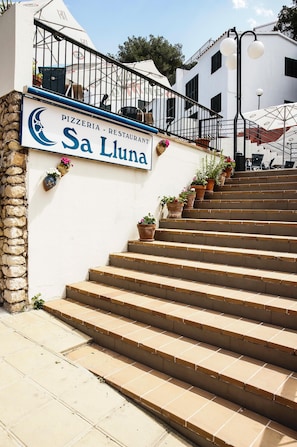 Eine Treppe führt zu einem Gebäude, an dem ein Schild für 'Pizzeria - Restaurant Sa Luna' angebracht ist.