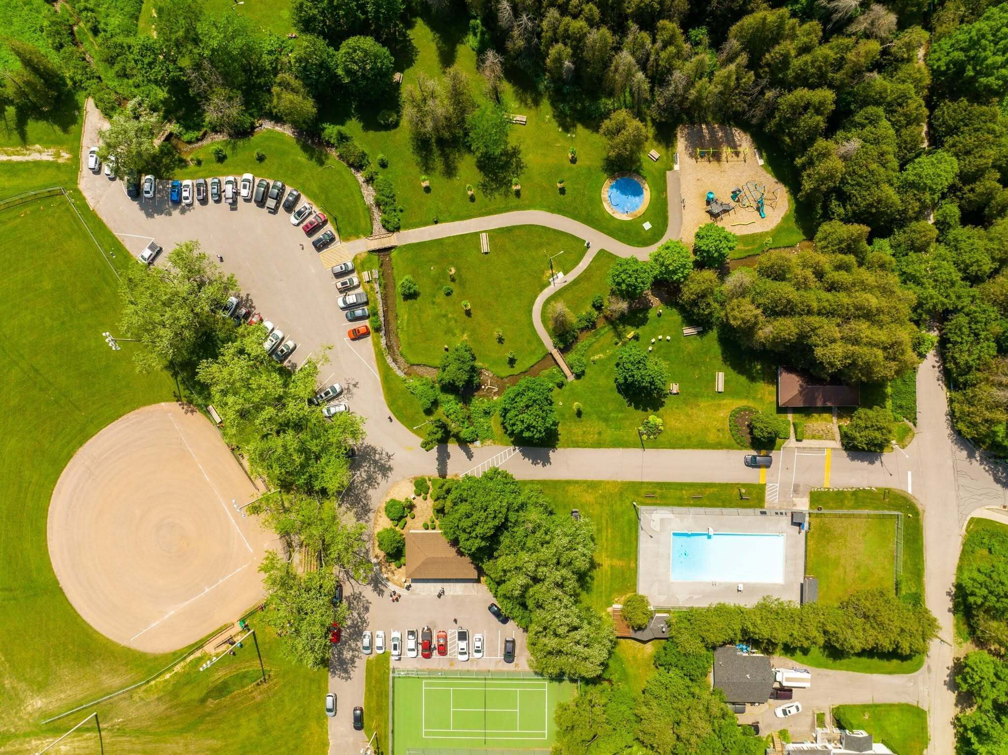 An aerial view of a residential area with a swimming pool, tennis court, and a parking lot.