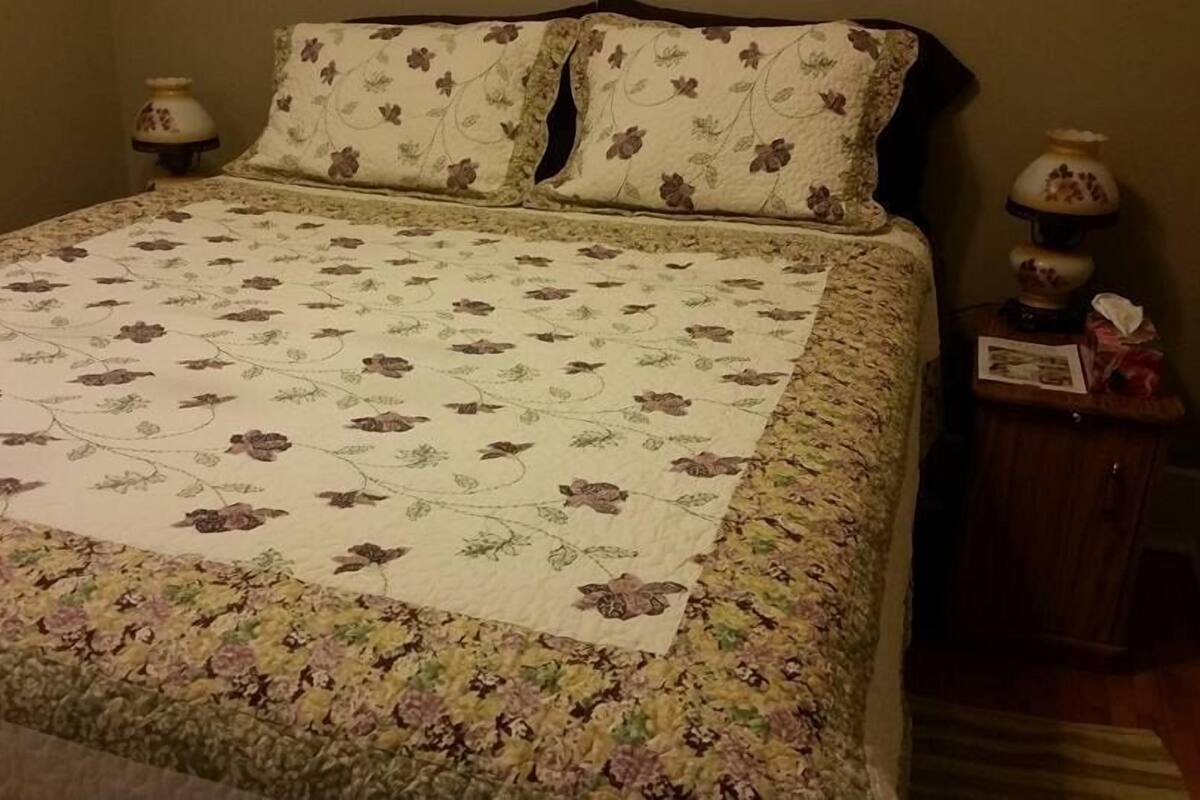 A bed with a floral quilt, two matching pillows, and two bedside lamps on a wooden nightstand.