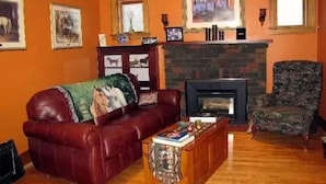 Una sala de estar con un sofá de cuero rojo, un sillón estampado, una chimenea y cuadros en las paredes.