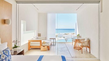 A modern hotel room with a large bed, a seating area with a view of the ocean, and a small table with chairs.