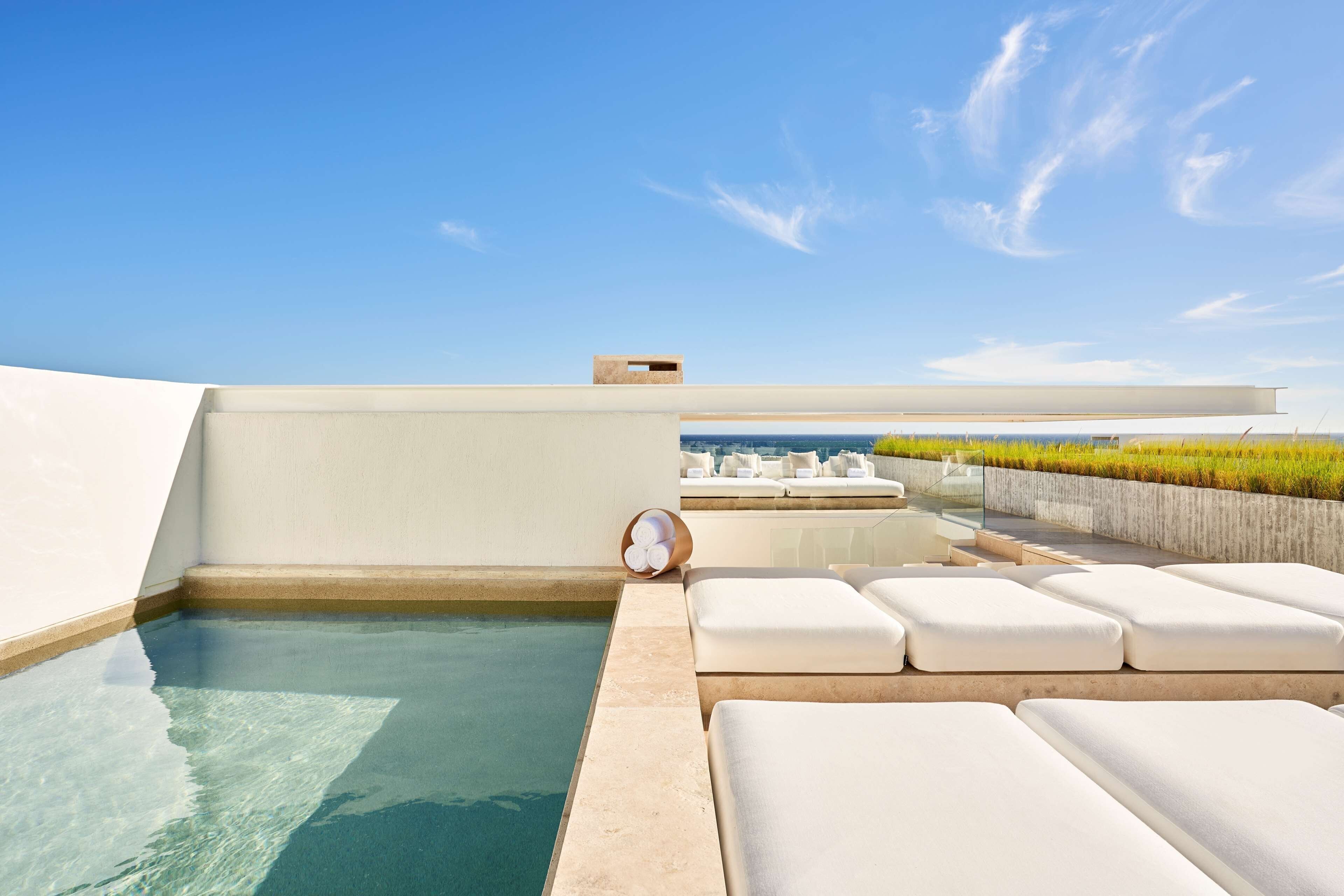 A rooftop pool area with clear blue water, white lounge chairs, and a view of the city skyline.