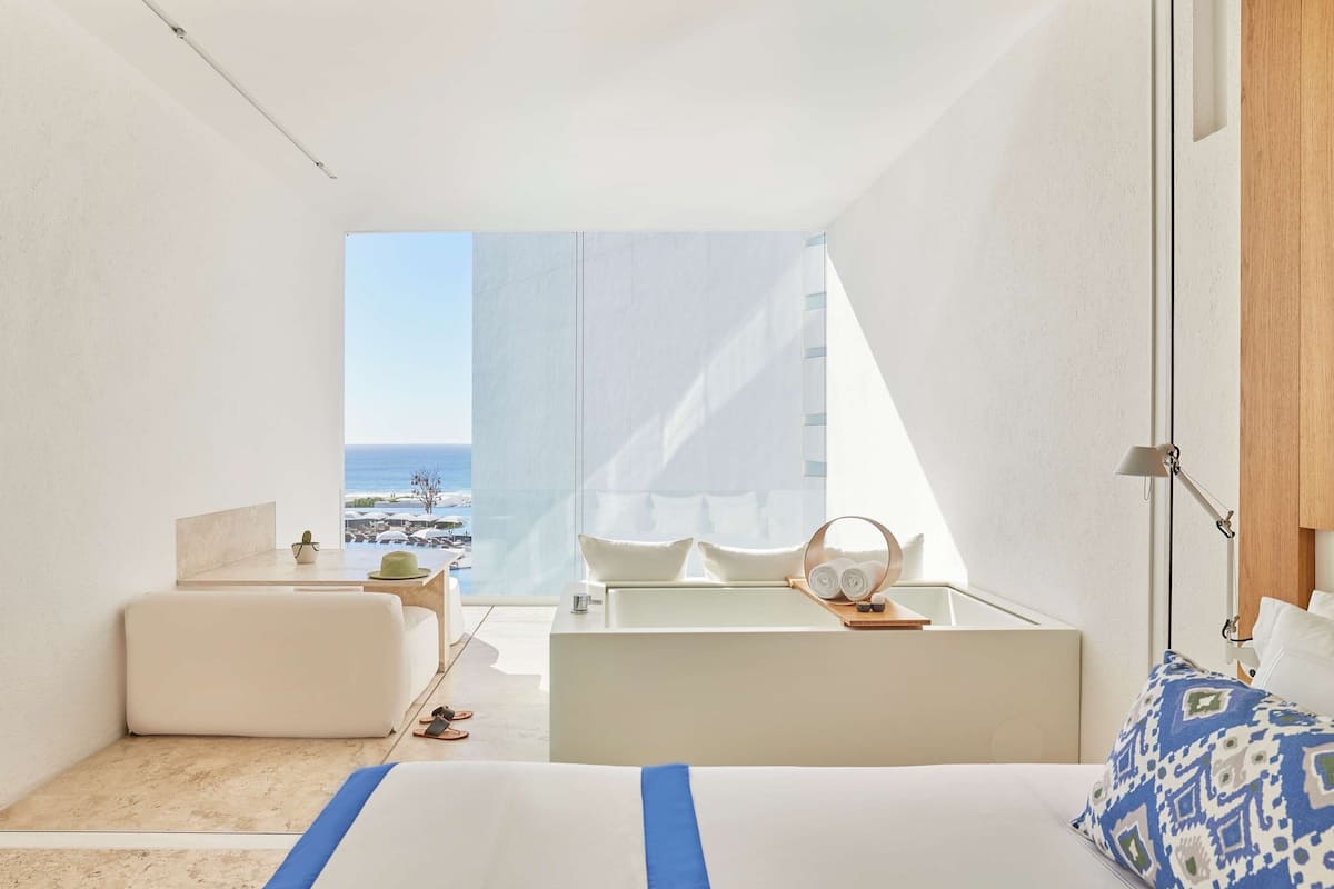 Una habitación de hotel moderna con cama, un rincón de descanso y vista al mar.