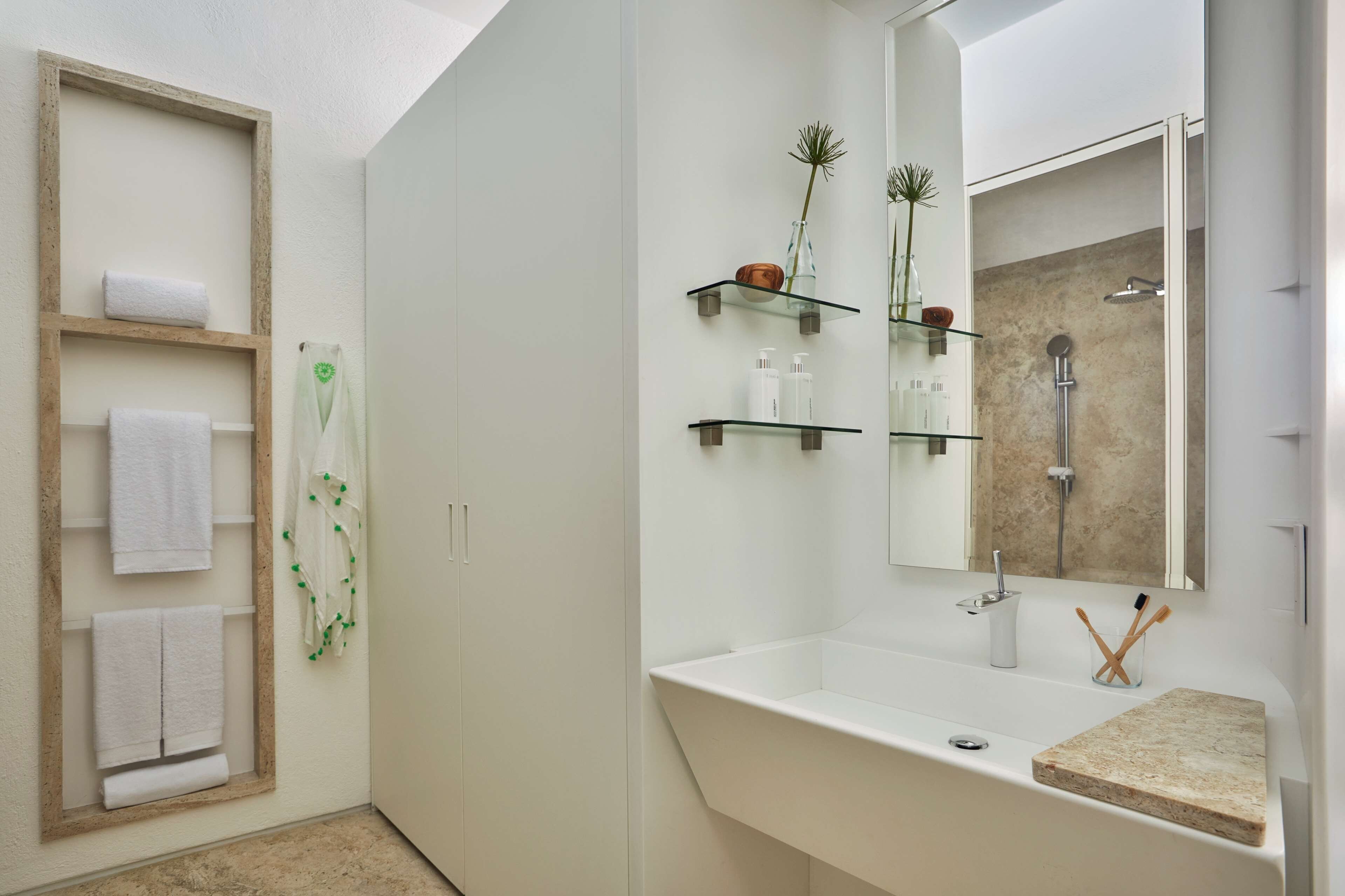 A modern bathroom with a white vanity, a glass shower enclosure, and a wooden towel rack.