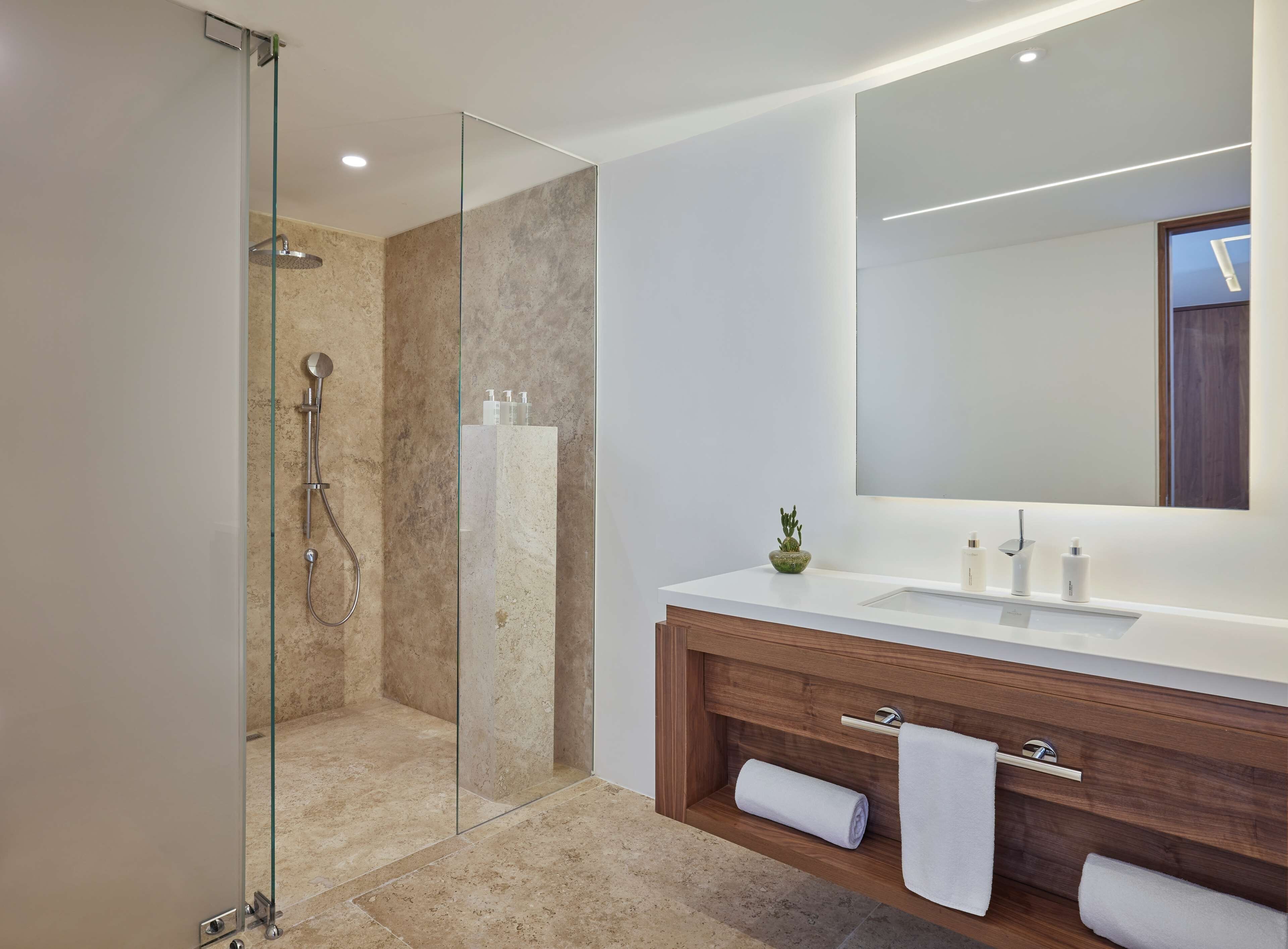 A modern bathroom with a glass-enclosed shower, a large mirror, and a wooden vanity with a sink and towel rack.