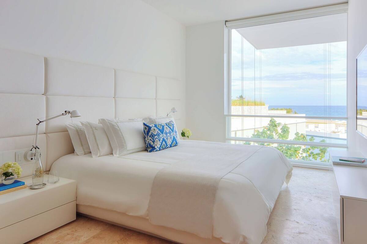 Un dormitorio moderno con una cama grande, ropa de cama blanca y vistas al mar a través de un ventanal.