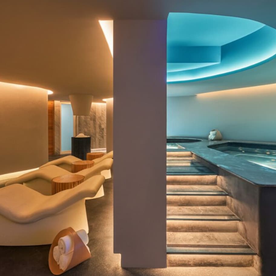 A modern spa with a hot tub, curved seating, and a staircase leading to a pool area.