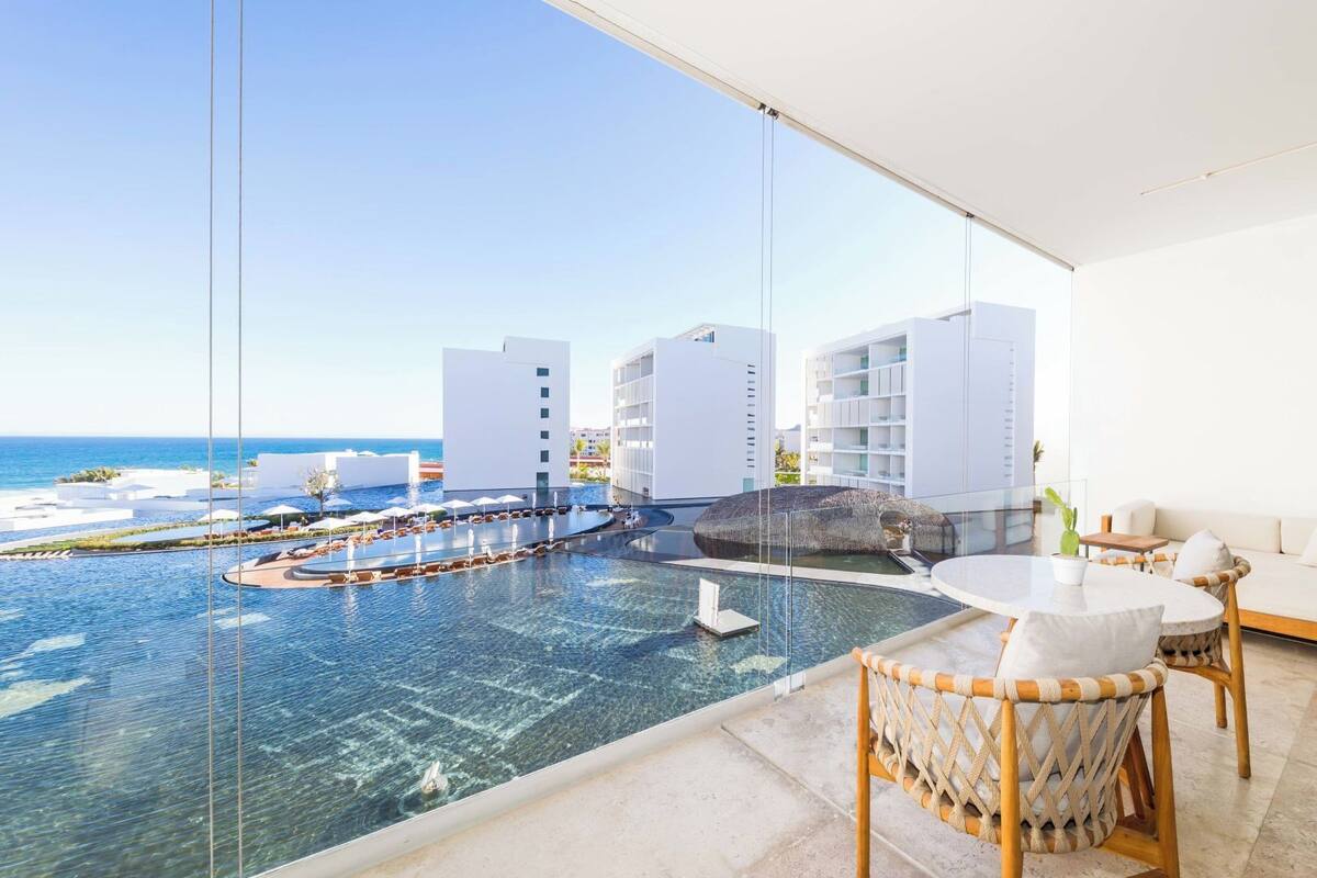 Habitación de hotel moderna con un amplio ventanal que da a una zona de piscina con varias fuentes y vistas al océano.