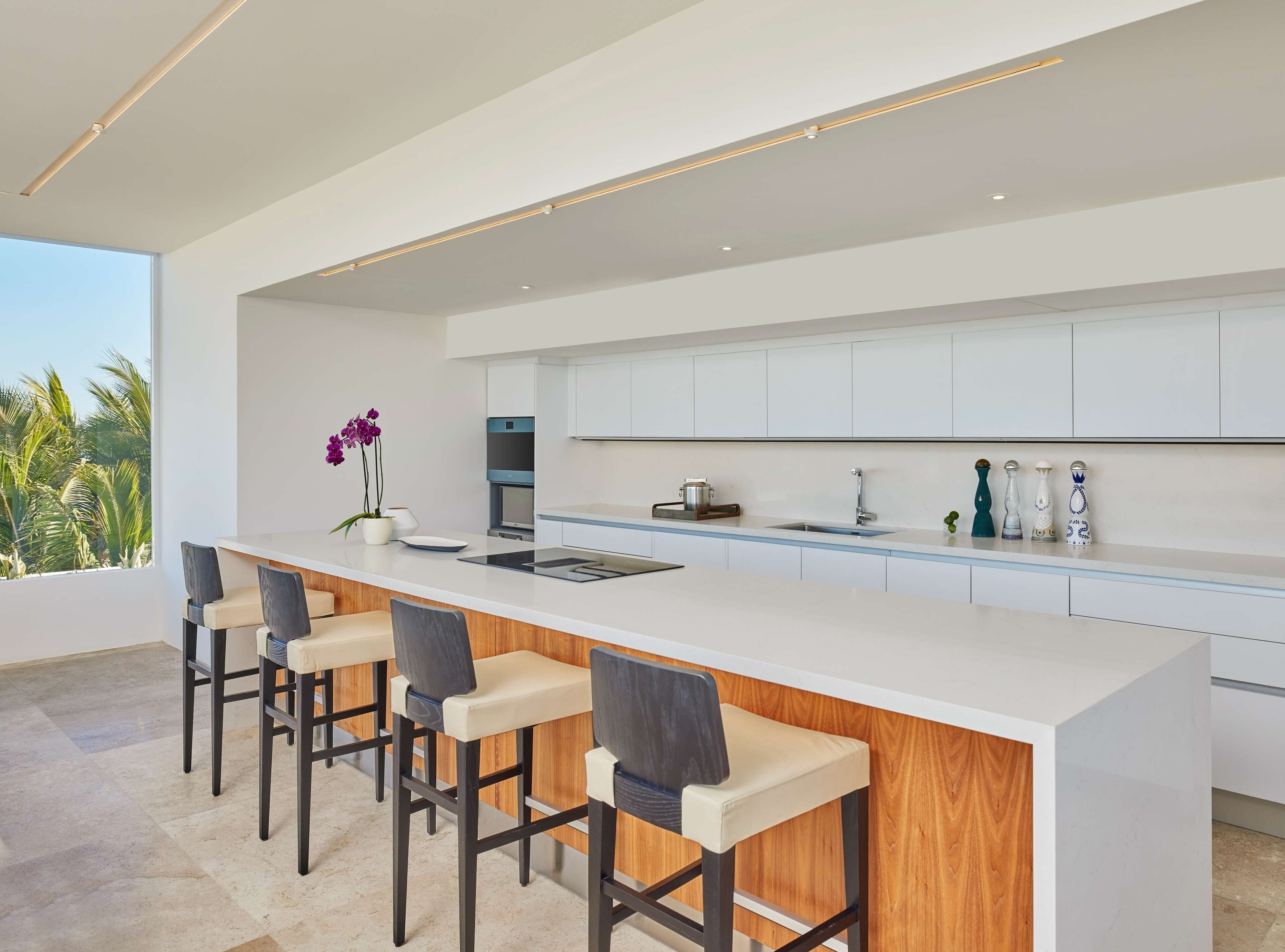 Een moderne keuken met een groot eiland, barkrukken en uitzicht op palmbomen.