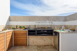 A compact kitchen with a built-in grill, wooden cabinets, and a countertop with various cooking utensils and ingredients.