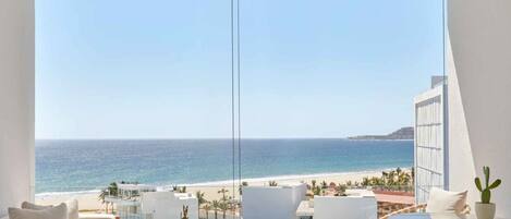 A modern hotel room with a large balcony overlooking a beach and ocean.