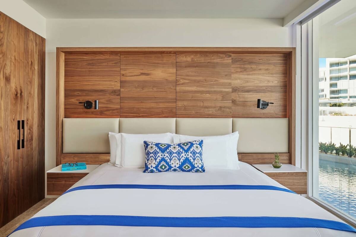 Habitación de hotel moderna con una cama grande, cabecero de madera y vista a una piscina.