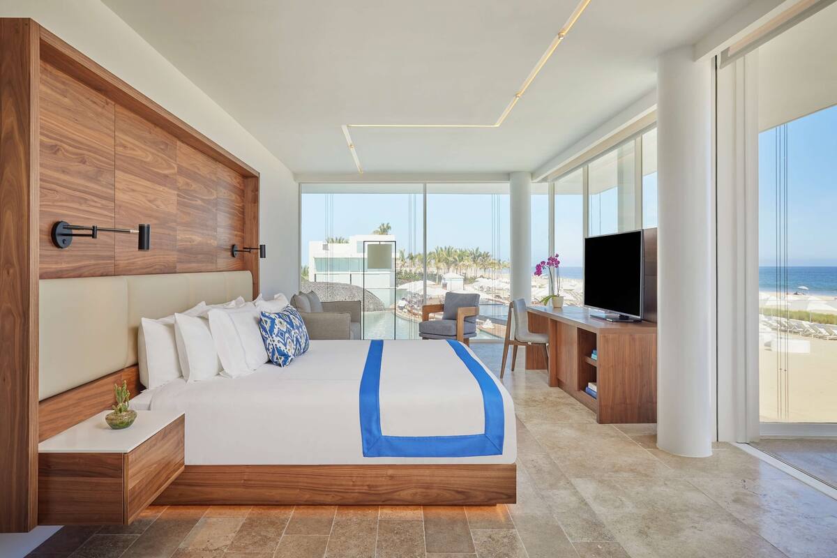Habitación de hotel moderna con una cama grande, un escritorio con televisor y vista a la playa.