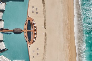 An aerial view of a beachside resort with a pool, lounge chairs, and a wooden deck.